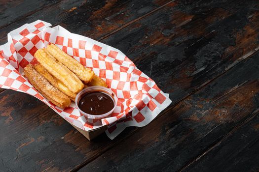 Churros with sugar powder in the box in paper tray, on old dark wooden table background with space for text, copyspace