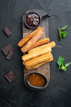 Typical Spanish snack churros, fried-dough pastry served usually with chocolate caramel hot sauce, on black background, top view flat lay