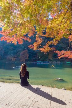 Tourist sitting and relaxing with beautiful nature view of Arashiyama in autumn season in Kyoto, Japan. Arashiyama is a one of attraction landmark for tourist in Kyoto, Japan