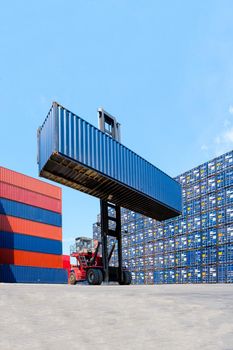 Forklift truck lifting cargo container in shipping yard or dock yard with cargo container stack in background for transportation import,export and logistic industrial concept.