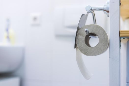 Toilet paper concept: Close up of toilet paper roll on chrome hanger, bathroom