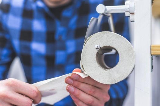 Toilet concept: male hands pulling toilet paper, close up