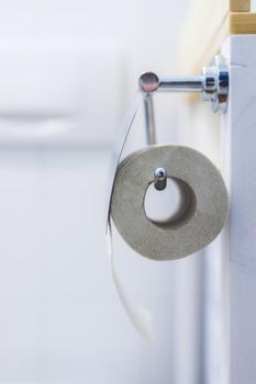Toilet paper concept: Close up of toilet paper roll on chrome hanger, bathroom