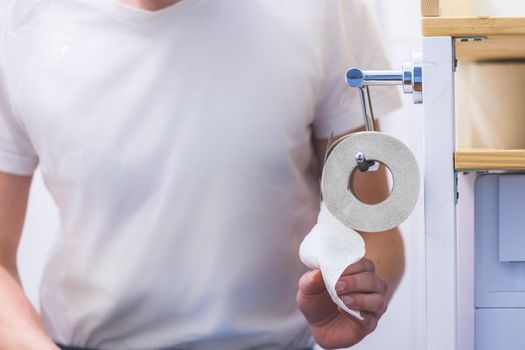 Toilet concept: male hands pulling toilet paper, close up