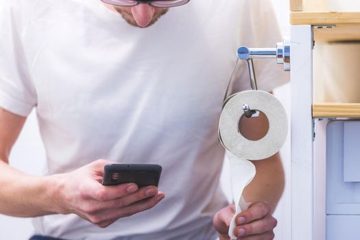 Pastime on the toilet: Young man using his smartphone while sitting on the toilet
