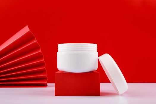 Selective focus, close up of opened jar with cream or mask on red pedestal against red background decorated with waver