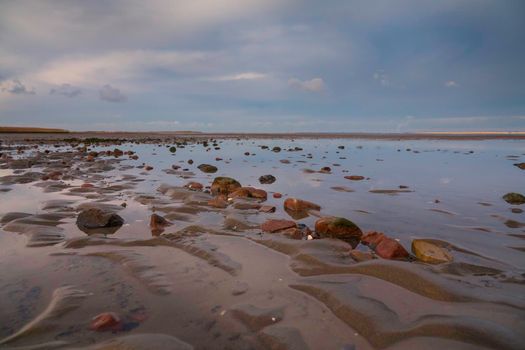 stones and water on the wet beach in Holland with cloudy sky as background