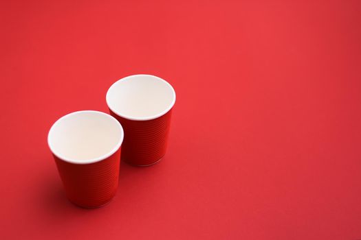 two red cardboard empty coffee glasses. two paper cups on red background.