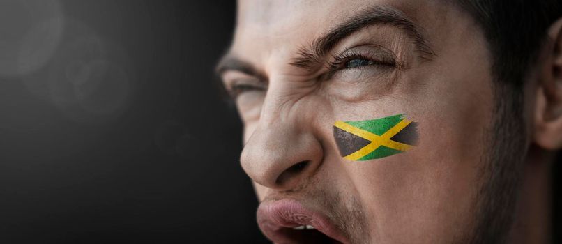 A screaming man with the image of the Jamaica national flag on his face