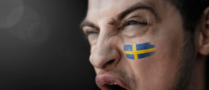 A screaming man with the image of the Sweden national flag on his face