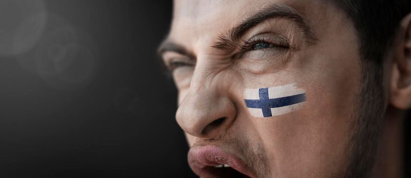 A screaming man with the image of the Finland national flag on his face