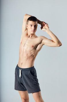 athlete in shorts with naked torso with joined hands behind head on gray background cropped view