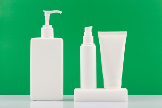 Set of beauty products for skin care in white unbranded tubes against green background. Concept of organic cosmetics