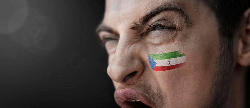 A screaming man with the image of the Equatorial Guinea national flag on his face