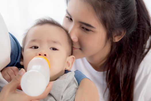 Young asian mother embracing and feeding little baby girl with bottle of milk at home, newborn innocence drinking with mom satisfied, relationship and bonding of mum and child, family concept.