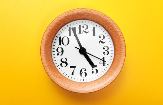 Wooden round clock on yellow background.