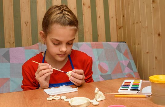 A girl at home paints figures from salt dough