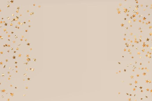 Stars golden glitter confetti isolated on blurred abstract beige background. Festive holiday background. Celebration concept. Falling magic gold particles. Invitation mock up. Top view, flat lay