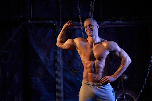 Young shirtless muscular man standing among metal chains, looking at camera, copy space