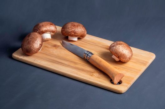 Parisian champignons, whole mushrooms on a cutting board on a black matte background. Organic food preparation concept.
