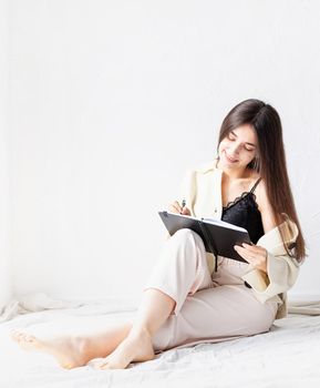 Beautiful woman in comfy home clothes writing notes sitting on the floor
