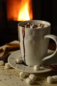 A cup of hot chocolate resting in front of a wood stove fire.
