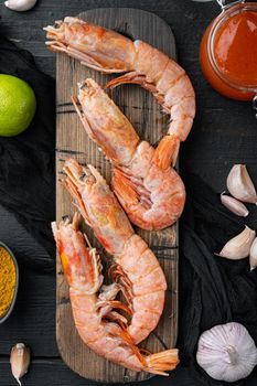 Raw king prawns or shrimps, on wooden cutting board, on black wooden table background, top view flat lay