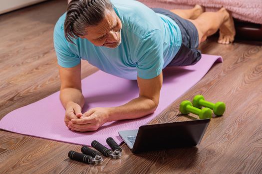 50 year old man performs exercises lying on mat at home looking at computer