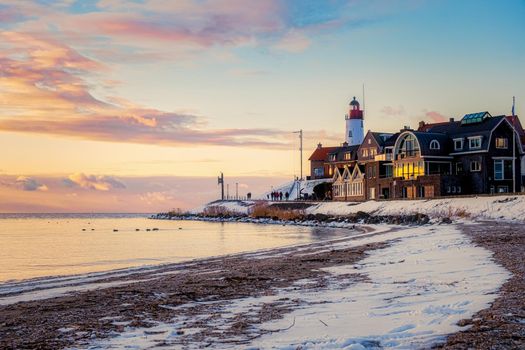 Winter in Urk with the dike and beach by the lighthouse of Urk snow covered during winter, sunset by the lighthouse of Urk Flevoland
