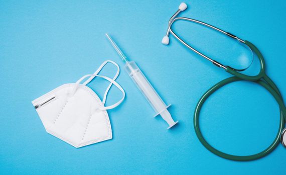 disposable medical mask, plastic syringe and stethoscope on blue background, top view