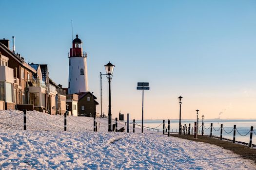 Winter in Urk with the dike and beach by the lighthouse of Urk snow covered during winter, sunset by the lighthouse of Urk Flevoland