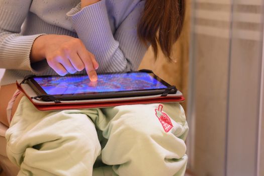 Child sitting on the toilet plays an online game on a tablet computer