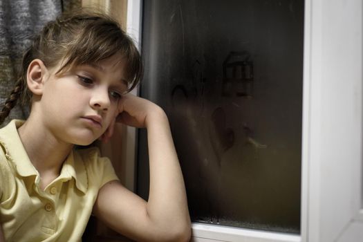 A frustrated girl sits at a foggy window and is sad