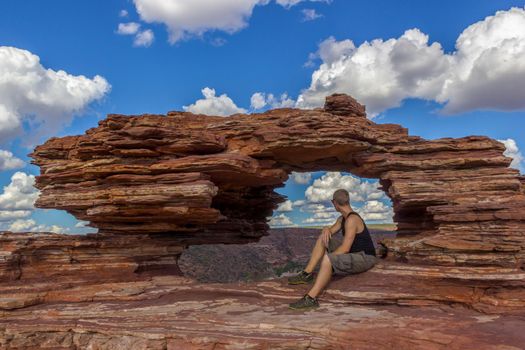 young man sitting in the Nature's Window, a natural arch rock formation in Kalbarri National Park on a sunny day