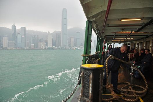 HONG KONG - 21th FEBRUARY, 2015: Sailing Star ferry in blue water of sea with Hong Kong cityscape in mist on background. View of ferry sailing in water with cityscape.