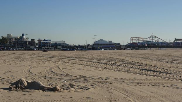 SANTA MONICA, LOS ANGELES CA USA - 19 DEC 2019 Alone anonymous man looks like unemployed and homeless sleeping on beach sand. Homelessness and begging crisis, social issue, poor people live on street