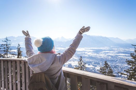 Happy young woman is raising her hands on the mountain, enjoying the view over Salzburg. Winter time on Gaisberg, Salzburg, Austria