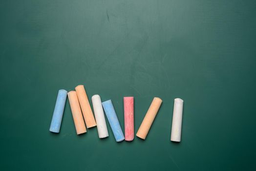 multicolored crayons on the background of green chalk school blackboard
