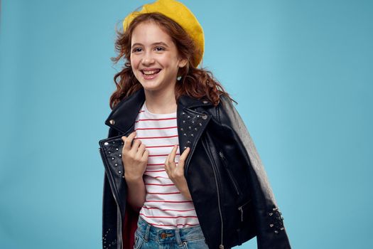 Fashionable girl in a yellow beret and leather jacket striped T-shirt blue background