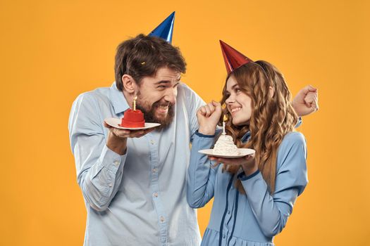 Man and woman at a party in caps and with tinsel cake fun yellow background