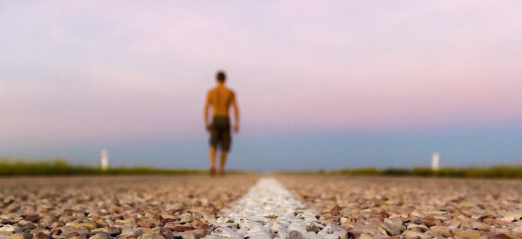 close up of road with young man walking on straight road through the outback of Australia, after a beautiful sunset, Nothern territory