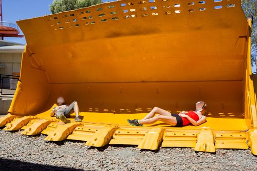 2 young people taking a nap in a mining front loader bucket for scale. Australia