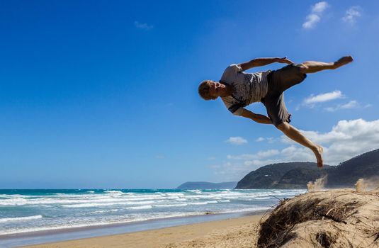 Portrait of young parkour man doing flip or somersault on the sand, Great Ocean Road, Australia