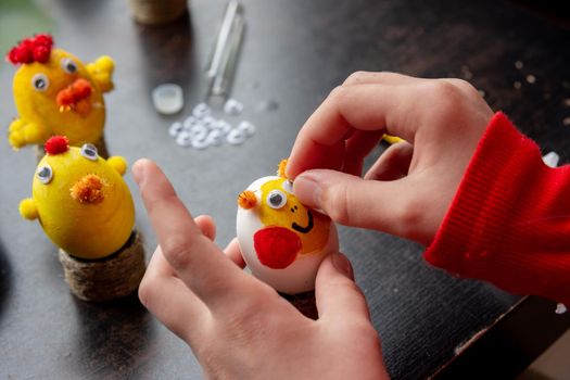 A girl decorates an egg for the Easter holiday by carefully gluing funny eyes to it
