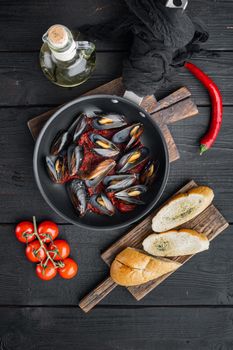 Mussels grilled with tomatoe sauce, on frying iron pan, on black wooden table background, top view flat lay