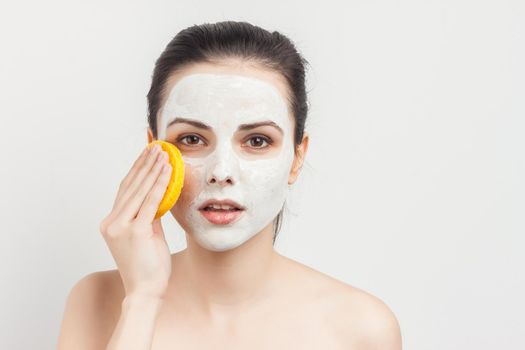 woman with bare shoulders with bum in hands removing mask from face