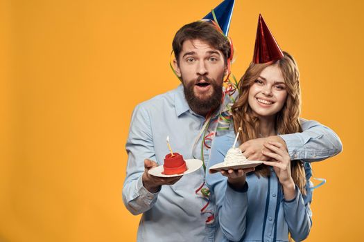 Energetic man and pretty woman with birthday cake in hats on a yellow background disco party. High quality photo