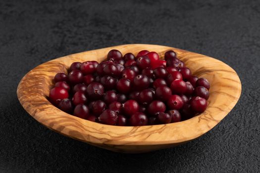 Ripe fresh cranberries in a wooden bowl on a black table