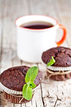 Fresh dark chocolate muffins with mint leaves and cup of tea on rustic wooden table.