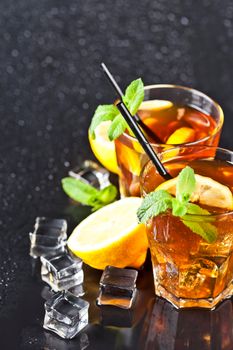 Two glasses with cold traditional iced tea with lemon, mint leaves and ice cubes